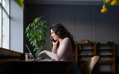 Kobieta rozmawia przez telefon, pracując przy laptopie. Dowiaduje się, jak dodać PKD do działalności, by rozszerzyć ofertę.