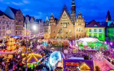 Tłoczny jarmark we Wrocławiu nocą, rozświetlony tysiącami lampek. Widać Ratusz, karuzelę i stragany.