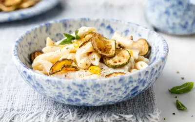 Piatto di pasta cremosa con ricotta e zucchine croccanti, guarnito con scorza di limone e menta.