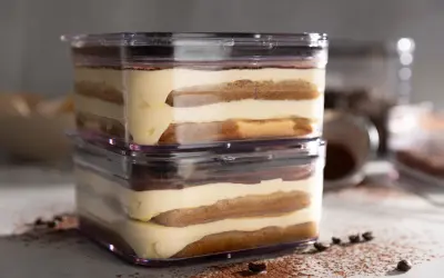 Zwei Schichten sally tiramisu im transparenten Behälter, mit Kakaopulver und Kaffeebohnen bestreut.