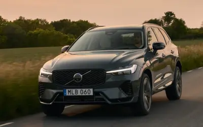 Ciemnoszary Volvo XC60 2025 jedzie drogą wśród zieleni o zachodzie słońca.
