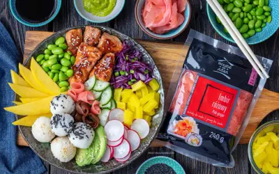Kolorowy bowl z lososiem, ryżowymi kulkami, mango, awokado, edamame i marynowanym imbirem. Obok opakowanie różowego imbiru.