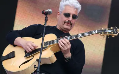 Un cantautore napoletano famoso con capelli bianchi e occhiali da sole suona una chitarra jazz.