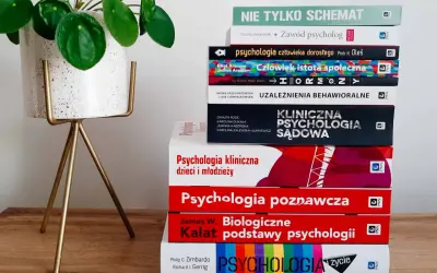 Stos książek o psychologii, w tym psychologia kliniczna, obok rośliny w doniczce.