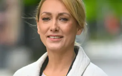 Portret uśmiechniętej blondynki w jasnym płaszczu.