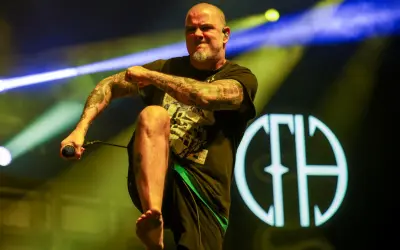 Phil Anselmo z Pantery w Polsce, z mikrofonem w dłoni, na tle sceny z oświetleniem.
