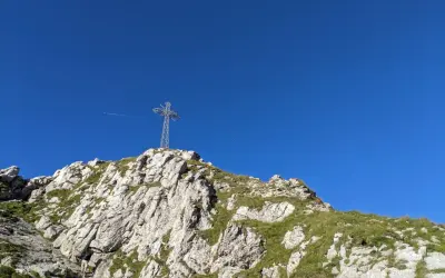 Kamienista trasa na Giewont, z widocznym krzyżem na szczycie i błękitnym niebem.