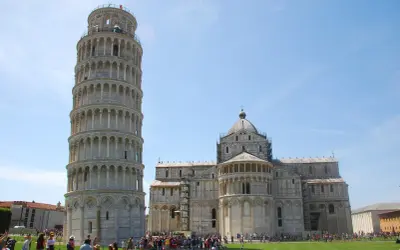 La Torre di Pisa si può salire, con la cattedrale sullo sfondo. Turisti ammirano la celebre struttura pendente sotto un cielo azzurro.