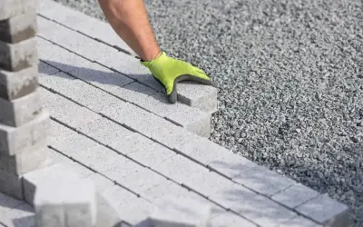 Dłoń w zielonej rękawicy układa kostkę brukową na podsypce. Właściwe podsypka pod kostkę brukową proporcje to klucz do trwałej nawierzchni.