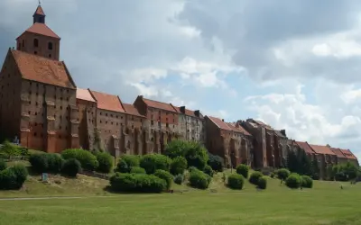 Grudziądz atrakcje: imponująca ceglana twierdza z wieżą i dachem z dachówki, otoczona zielenią i trawnikiem.