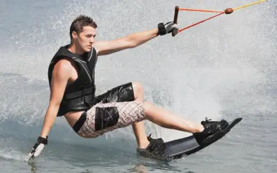 Młody mężczyzna na desce, ciągnięty przez linę, pokazuje, **wakeboarding co to** jest – sport wodny pełen adrenaliny i zabawy.