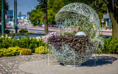 Ozdobna kula z kwiatami, przykład instalacji artystycznej. Wplecione w ażurową konstrukcję rośliny tworzą efektowną kompozycję.
