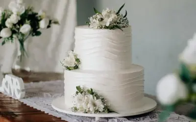 Elegancki tort komunijny, idealny na 20 osób. Białe kwiaty zdobią dwupoziomowe ciasto.