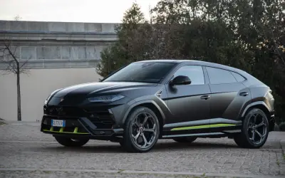 Un imponente **lamborghini urus negro** se exhibe con detalles en verde lima, posado sobre un camino empedrado.