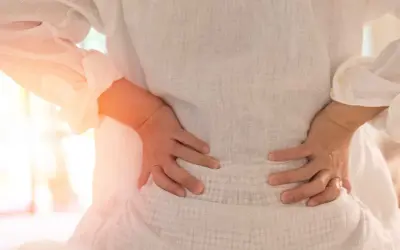 Gravid kvinna med ryggskott håller sig om ländryggen. Smärtan lyser orange.