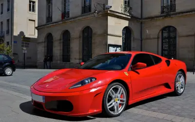 Czerwone Ferrari F430 na brukowanej ulicy przed kamienicą. Zastanawiasz się, ile kosztuje Ferrari? To marzenie wielu kierowców.