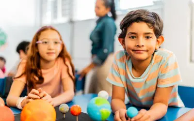 Kinder lernen spielerisch über das Sonnensystem. Ein Junge hält eine Himmelskugel, während ein Mädchen mit einem Modell des Sonnensystems experimentiert. Dies sind Beispiele für alternative Schulkonzepte.
