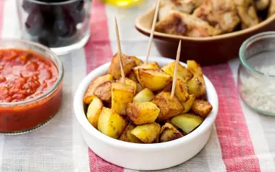 Patatas bravas dorées, servies avec une sauce tomate épicée et des olives. Un délice pour l'apéro !