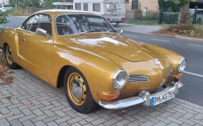 Złoty Karmann Ghia, klasyk z lat 60., lśni na tle ulicy.