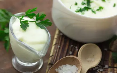 Cremige Bechamel-Sauce in einer Sauciere, garniert mit Petersilie. Daneben eine Schüssel mit der Sauce und grobes Salz auf Holzlöffeln.