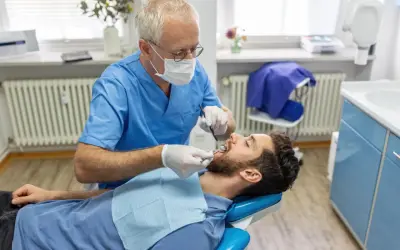Dentysta bada pacjenta. Zastanawiasz się, ile kosztuje usunięcie ósemki na NFZ? Wizyta u stomatologa to pierwszy krok.