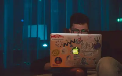 Chłopak z okularami szuka angielskich nicków do gier na laptopie ozdobionym naklejkami.
