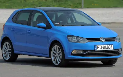 Niebieski VW Polo 2010 z czarnym dachem, zaparkowany na zewnątrz. Kierowca siedzi za kierownicą.