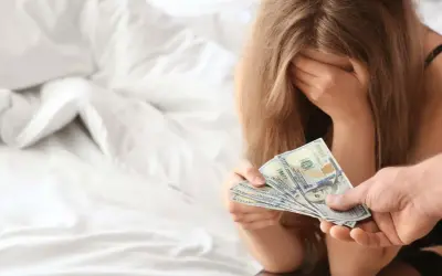 Kobieta z ręką na twarzy otrzymuje pieniądze. To obrazuje problem sutenerstwa i tego, co to znaczy.