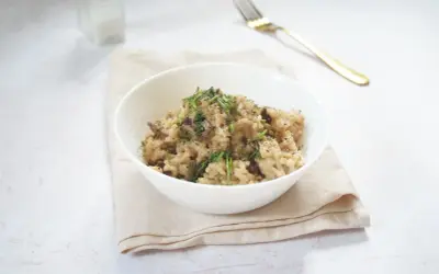 Miseczka kremowego risotto z grzybami, posypana ziołami, na jasnym obrusie.