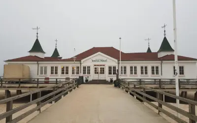 Historyczna budowla na molo w Ahlbecku, z charakterystycznymi zielonymi dachami i białymi ścianami, zaprasza do spaceru.