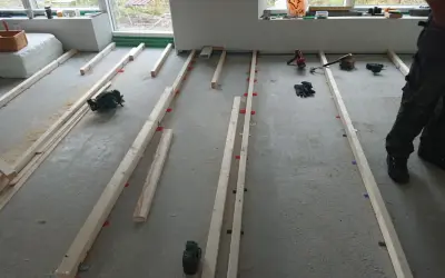 Arbetare förbereder för att regla upp golv med träreglar och verktyg som cirkelsåg och skruvdragare.
