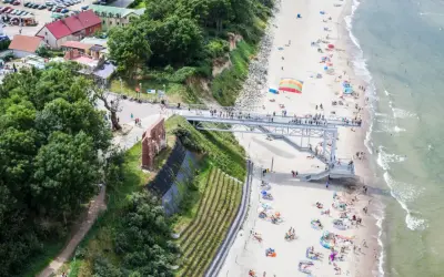 Widok na plażę z kładką i ruinami. Ludzie odpoczywają na piasku, ciesząc się atrakcjami nad morzem.