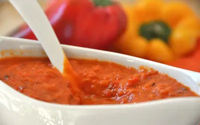 Crema di peperoni bimby in una ciotola bianca, con peperoni rossi e gialli sfocati sullo sfondo.