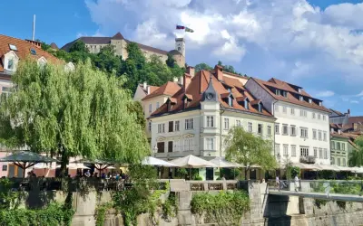 Urokliwy widok na rzekę i zabytkowe kamienice w Słowenii, Lublana. W tle widać zamek na wzgórzu.