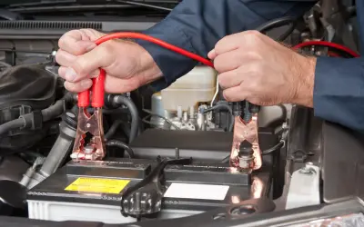 Ręce mechanika podłączają kable rozruchowe do akumulatora samochodowego, rozpoczynając czas ładowania akumulatora.