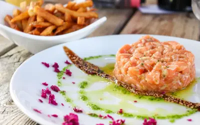 Tatar z łososia do sushi, podany z sosem i posypką z sezamu, obok miseczki frytek.