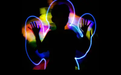 Silueta de niño jugando con light painting, creando auras de colores vibrantes a su alrededor.