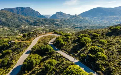 Ein Rennradfahrer auf Kreta genießt die kurvenreiche Straße durch eine grüne Berglandschaft.