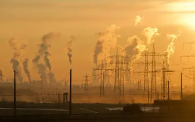 Dymiące kominy fabryk i linie energetyczne na tle zachodzącego słońca symbolizują antropogeniczne zmiany klimatu.