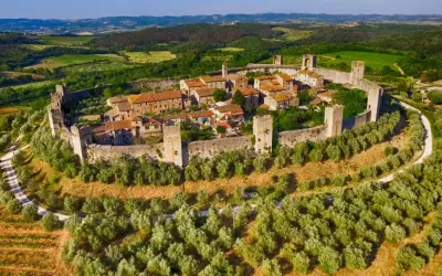 Borgo medievale fortificato su una collina, circondato da uliveti e vigneti. Bellissimi paesaggi toscani sotto un cielo azzurro.