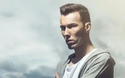 Dorian Tomasiak w szarej bluzie z kapturem i białej koszulce, z burzą chmur w tle.