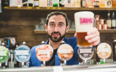 Barista con una birra in mano, pronto a versare nei bicchieri. Dietro di lui, una selezione di birre artigianali.