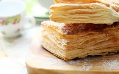 Chrupiące ciastka z ciasta francuskiego, posypane cukrem pudrem, czekają na filiżankę kawy.