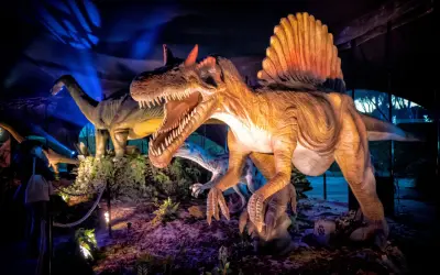 Figuras de dinosaurios realistas, incluyendo un Spinosaurus con su vela dorsal, en una exhibición nocturna en Madrid.