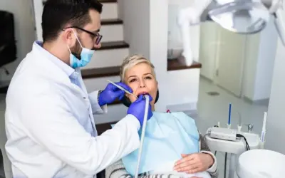 Dentysta wykonuje piaskowanie zębów u pacjentki, która siedzi na fotelu dentystycznym.