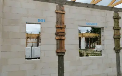 Budowa domu z bloczków betonowych, widoczne okna i drzwi z tymczasowym nadprożem, drewniane elementy konstrukcyjne.