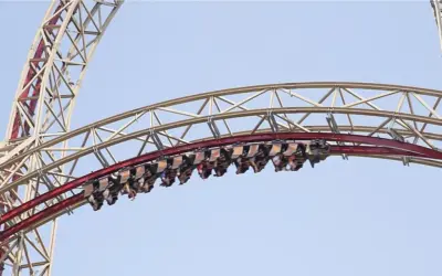 Wagoniki rollercoaster w Polsce pędzą po czerwonym torze na tle błękitnego nieba.