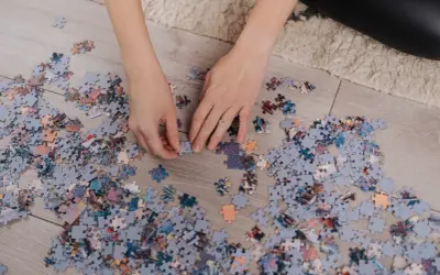 Ręce układają puzzle na podłodze. Po skończeniu dowiesz się, jak powiesić puzzle na ścianie.