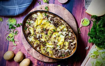 Herzhafter kartoffelauflauf mit hackfleisch, überbacken mit Käse und garniert mit Petersilie. Dazu frische Kartoffeln, Lauch und ein Stück Käse.