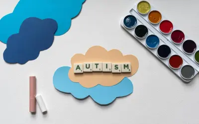 Litery układają słowo AUTISM na chmurce. Obok kredki i farby. Dzieci z autyzmem wysokofunkcjonującym mogą rozwijać się twórczo.